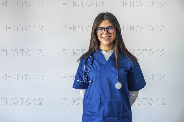 Female doctor in blue scrubs with stethoscope, smiling confidently at camera on white background, professional, friendly healthcare provider representing care and trust in clinical setting
