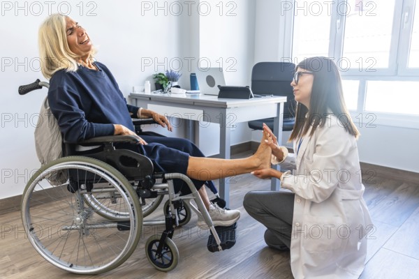 Female doctor examining and rehabilitating a senior woman's leg and ankle, who is seated in a wheelchair and experiencing pain during physical therapy session