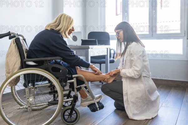Doctor examining a patient's leg and ankle, the patient sitting in a wheelchair during a consultation for physical therapy or rehabilitation in a clinic or hospital
