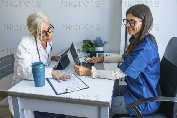 Female physician and junior nurse collaborate in a modern clinic office, reviewing patient data on laptop and tablet to illustrate teamwork, digital healthcare, mentorship and research