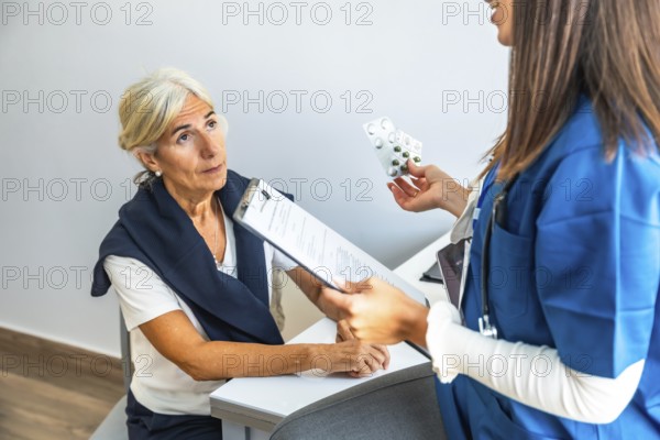 Healthcare professional explaining medication to an attentive elderly patient during annual check up, holding a blister pack of pills and medical forms
