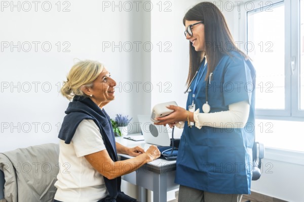 Doctor talking to senior woman, holding a blood pressure monitor, and preparing to check her vitals during a healthcare consultation in a bright clinic setting