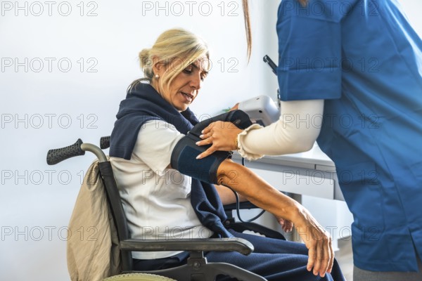 Medical professional monitoring the vital signs of an elderly patient with a blood pressure cuff while she sits in a wheelchair, providing healthcare and support