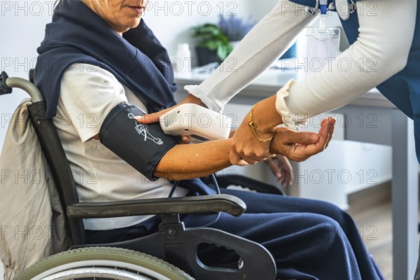 Healthcare professional measuring blood pressure of an elderly woman in a wheelchair, providing routine vital sign monitoring and compassionate medical support during a clinic visit