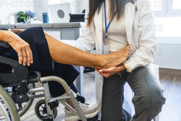 Healthcare professional wearing a lab coat and examining the leg of a senior patient sitting in a wheelchair, providing medical care and rehabilitation in a clinical setting