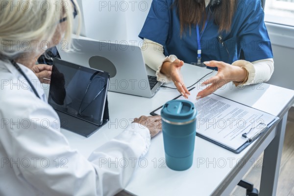 Healthcare professionals discussing medical information during a consultation in an office with a laptop, tablet, and documents, representing modern medicine and technology in health services