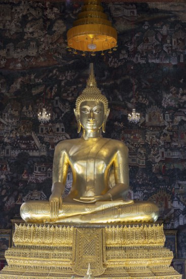 Golden Buddha statue, Phra Buddha Trilokachet surrounded by crystal chandeliers and exquisite wall paintings, interior view of Phra Ubosot or ordination hall, Wat Suthat Thepwararam, Royal Temple, Phra Nakhon, Bangkok, Thailand