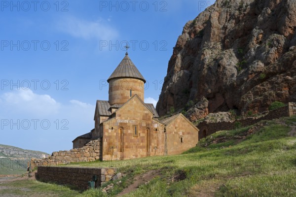 A stone monastery building rising on rough rock walls, surrounded by blue skies and green meadows, Noravank monastery, Surb Karapet baptism church, Noravank, Vayots Dzor province, Wajoz Dzor, Armenia, Caucasus