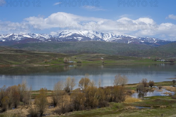 Peaceful landscape with a lake surrounded by snow-capped mountains. Trees and meadows dot the shore under a blue sky with scattered clouds, Imranli Reservoir, Imranli, Kizilirmak River, Kizilirmak, Sivas Province, Turkey