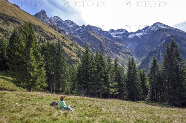 Young woman sitting in a meadow and looking at the mountains of the Allgäu Alps with Trettachspitze, Mädelegabel, Hochfrottspitze, Wilder Mann and Linkerskopf, Einödsbach, Oberstdorf, Oberallgäu, Bavaria Germany