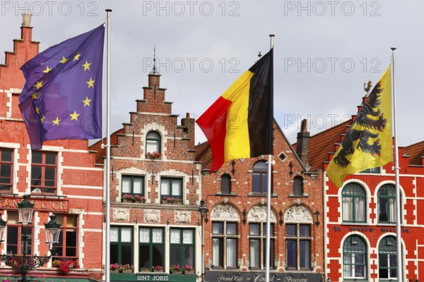 Historic houses on the market square in the old town of Bruges, Grote Markt, former guild houses, now restaurants and cafes, flags of Europe, Belgium, Flanders (from left to right), UNESCO World Heritage Site, Flanders, Belgium