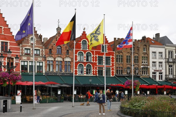 Historic houses on the market square in the old town of Bruges, Grote Markt, former guild houses, now restaurants and cafes, flags of Europe, Belgium, Flanders and Bruges (from left to right), UNESCO World Heritage Site, Flanders, Belgium