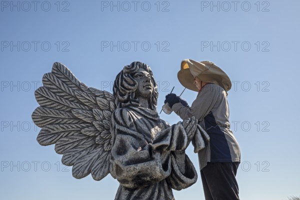Chandler, Minnesota, Artist Primi Monteiga re-paints her concrete sculpture of an angel in the midst of Minnesota cornfields. Born in Spain, Monteiga grew up in Venezuela where she is well known for her art. She has been living in rural Minnesota since 2010