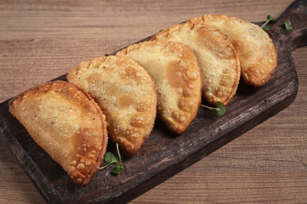 Fried chebureks, deep-fried, mini, on a chopping board, wooden table, close-up, no people