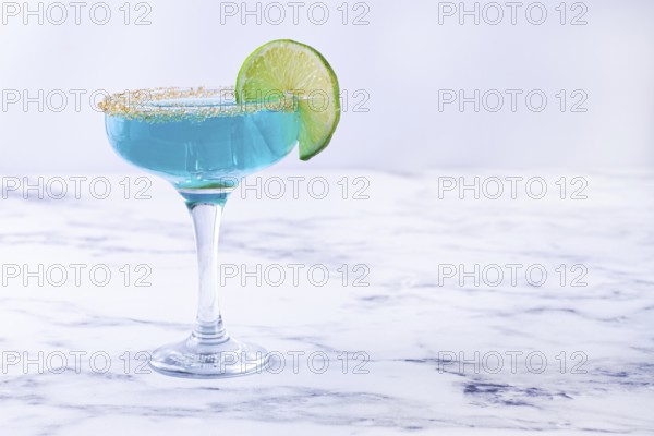 Bright blue cocktail with a slice of lime on a marble surface