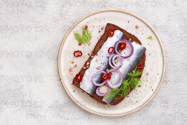 Sandwiches, Herring fish, on dark rye bread, sprinkled with onion, chili pepper and herbs, on a light plate