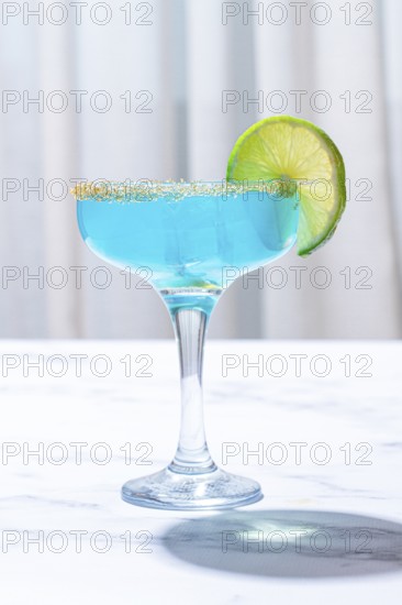Bright blue cocktail with a slice of lime on a marble surface