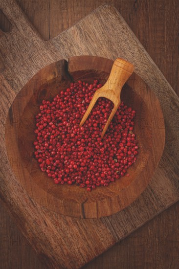 Bright red peppercorns, in a wooden bowl, with a small wooden tray