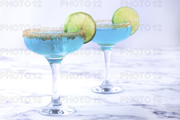 Colorful blue cocktails in elegant glasses with lime garnish on a marble table