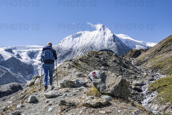Female hiker with hiking sticks on a rocky slope with a view of snow-covered mountain peaks, Mont Blanc de Cheilon mountain summit with glacier, Hérménence, Valais Alps, Switzerland