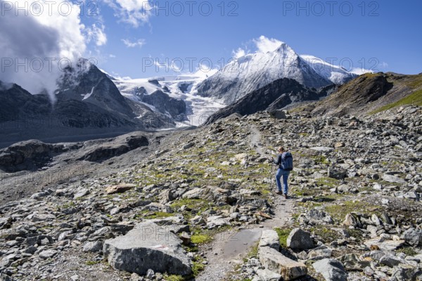Hiker on rocky path with impressive views of snow-covered mountain landscape, Mont Blanc de Cheilon mountain summit with glacier in the back, Hérménence, Valais Alps, Switzerland