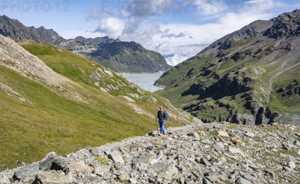 Hiker in a wide mountain landscape with a view of valley and lake, surrounded by green hills, Mont Blanc de Cheilon mountain summit with glacier in the back, Hérménence, Valais Alps, Switzerland