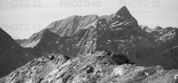 Gamsjoch summit cross in front of dramatic mountain panorama in black and white, Dreizinkenspitze and Laliederer Wand, eastern Karwendel, Tyrol, Austria