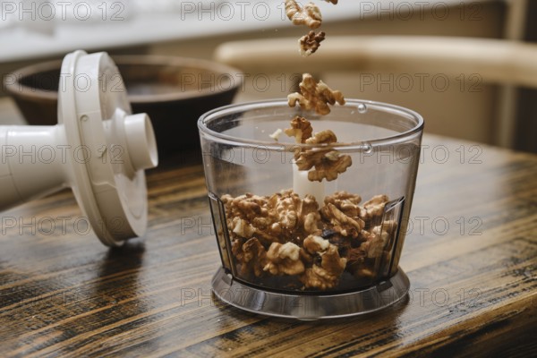 A person is preparing to chop walnuts using a food processor in a cozy kitchen. The walnuts are flying into the container, showcasing an active cooking moment