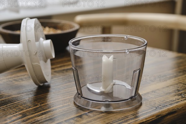 A clear food processor bowl on a rustic wooden table, ready for use. Nearby, the processor's motor base awaits. Perfect for preparing meals or snacks at home in a cozy kitchen setting