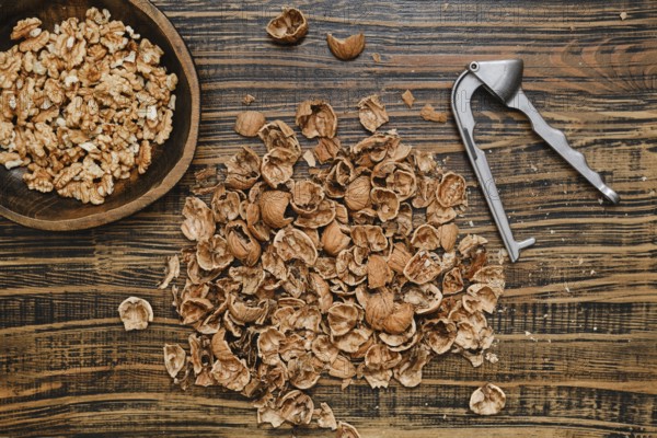 Walnuts are being shelled on a rustic wooden surface. A bowl of walnut pieces sits nearby, while the shells are scattered around, showcasing the process of nut preparation in a cozy kitchen setting