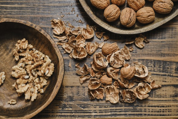 Whole walnuts and broken shells scattered across a wooden table. Some walnut pieces are neatly placed in a separate wooden bowl, showcasing their natural beauty