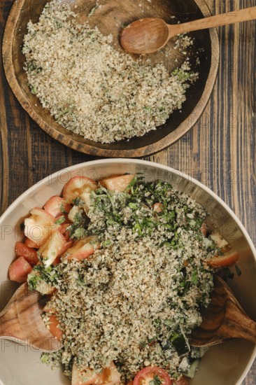 A colorful salad made with fresh tomatoes, cucumber, greens, and a topping of chopped nuts in a wooden bowl. A second bowl holds additional nuts