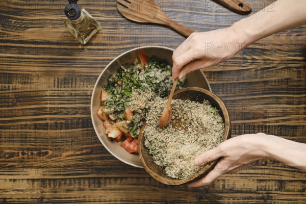 Adding ground walnuts to a bowl with chopped vegetables and herbs. A wooden spoon is used to combine the fresh ingredients. Olive oil and utensils can be seen in the background