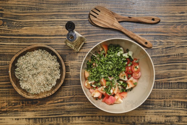 Chopped tomatoes and fresh herbs in a bowl ready for mixing. A bowl with crushed walnuts is nearby, alongside wooden utensils on a rustic wooden table