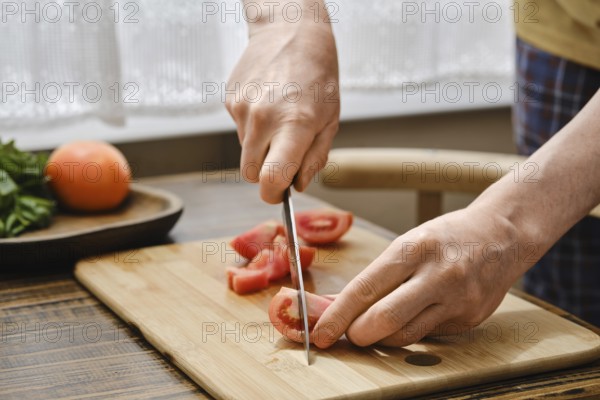 Hands skillfully slice fresh tomatoes on a wooden cutting board while preparing a delicious meal in a bright, cozy kitchen. The scene captures the joy of cooking with fresh ingredients