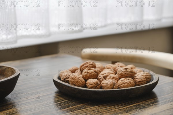 A wooden bowl filled with fresh walnuts on a rustic table in a bright, airy kitchen. Soft natural light filters through a nearby window, highlighting the textured surface of the nuts