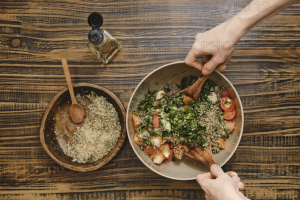 Hands gently mix fresh tomatoes, herbs, and chopped walnuts in a large bowl. Wine vinegar oil is nearby for drizzling over the salad