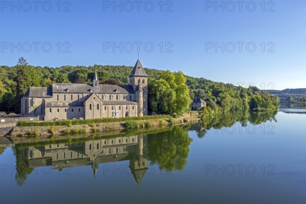 Abbey Church of St Peter, Église abbatiale Saint-Pierre d'Hastière, Hastière-par-delà reflected in water of the river Meuse, Namur, Wallonia, Belgium