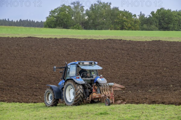 Tractor with plough, agricultural ploughing machine working on a field in autumn, fall in the Belgian Ardennes, Luxembourg, Wallonia, Belgium