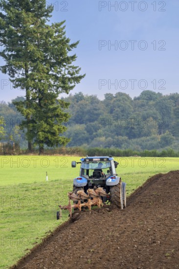 Tractor with plough, agricultural ploughing machine working on a field in autumn, fall in the Belgian Ardennes, Luxembourg, Wallonia, Belgium