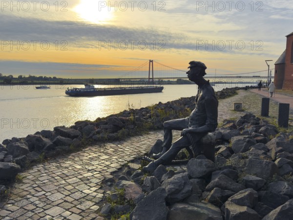 Photo with melancholy mood of bronze sculpture Poortekerl looking at Rhine waiting for ship to unload, Rhine navigation inland shipping, reminiscence of old times, bronze statue by artist Heide Friede-Kinalzik, Emmerich, Lower Rhine, North Rhine-Westphalia, Germany