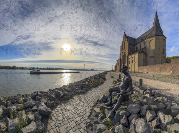 Photo with melancholy mood of bronze sculpture Poortekerl looking at Rhine waiting for ship to unload, Rhine navigation inland navigation, reminiscence of old times, bronze statue by artist Heide Friede-Kinalzik, rebuilt church of St. Martini destroyed in the Second World War, Emmerich, Lower Rhine, North Rhine-Westphalia, Germany