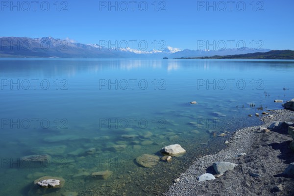 Clear blue water with rocks on the shore and snowy mountains in the background, Lake Pukaki Viewpoint, Pukaki, Canterbury, South Island, New Zealand