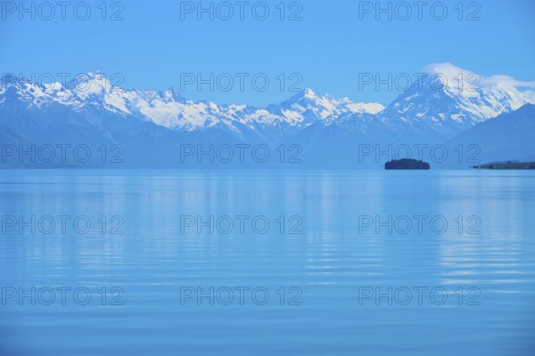 Expansive view of a tranquil lake with snow-capped mountains Mount Cook and an island, Lake Pukaki Viewpoint, Pukaki, Canterbury, South Island, New Zealand