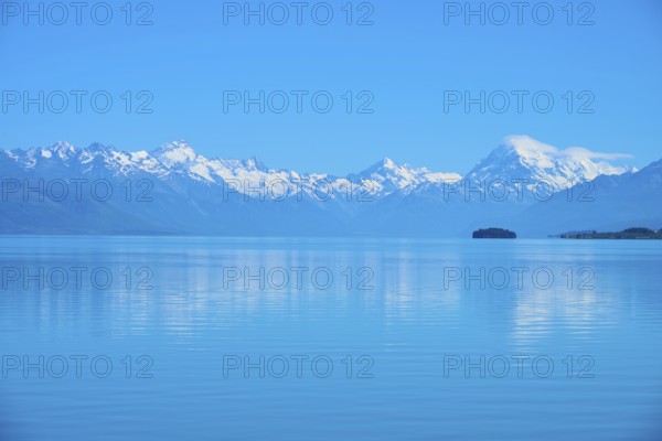 Mount Cook snow-capped mountains are reflected in a calm, blue lake, Lake Pukaki Viewpoint, Pukaki, Canterbury, South Island, New Zealand