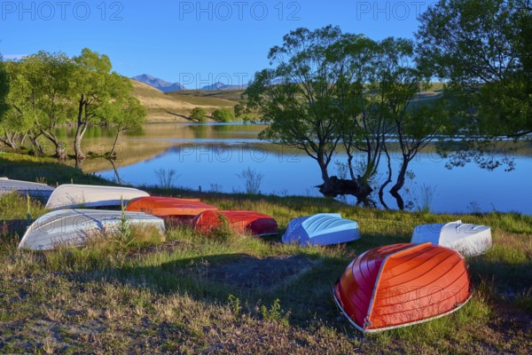 Boats on the shore of a calm lake at dusk with reflecting mountains in the background, Lake McGregor, Tekapo, Canterbury, South Island, New Zealand
