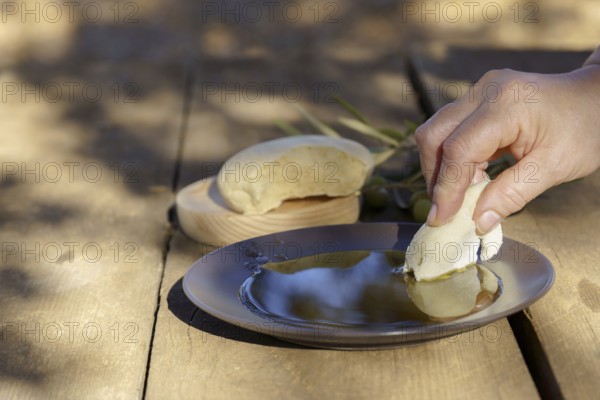 Hand dipping fresh homemade bread into healthy extra virgin olive oil, a staple of homemade mediterranean diet and cuisine