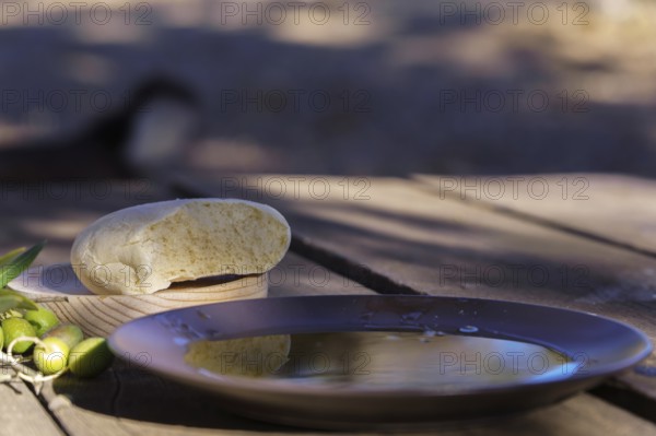 Extra virgin olive oil in a bowl, bread, and green olives on a rustic wooden table capturing mediterranean cuisine