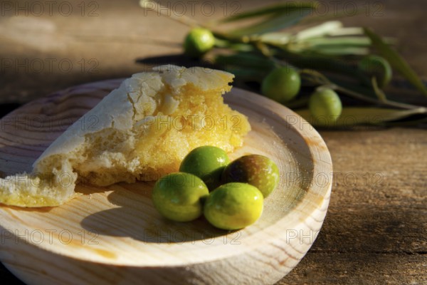 Rustic bread dipping in extra virgin olive oil served with fresh green olives on a wooden background, representing mediterranean cuisine