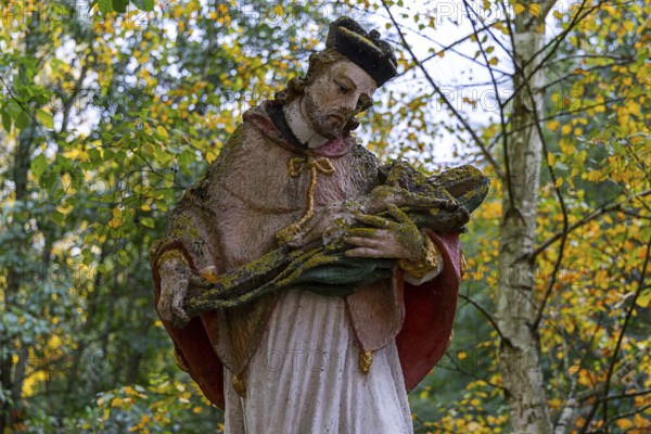 Close-up of a religious statue with a cape in an autumnal park, covered by moss, Weinviertel Lower Austria